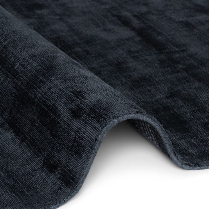 Close-up of a textured dark gray rug corner on a white background