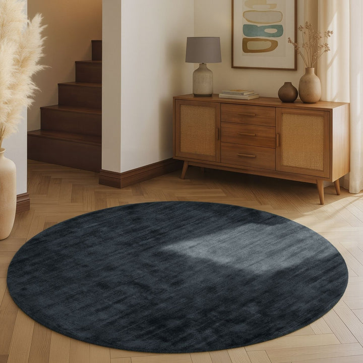 Round dark blue rug on a wooden floor with a wooden cabinet and decorative items in the background.