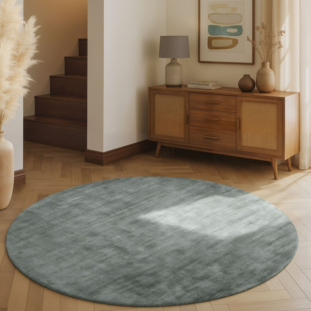 Round gray rug on a wooden floor with a wooden sideboard and decorative items in the background.