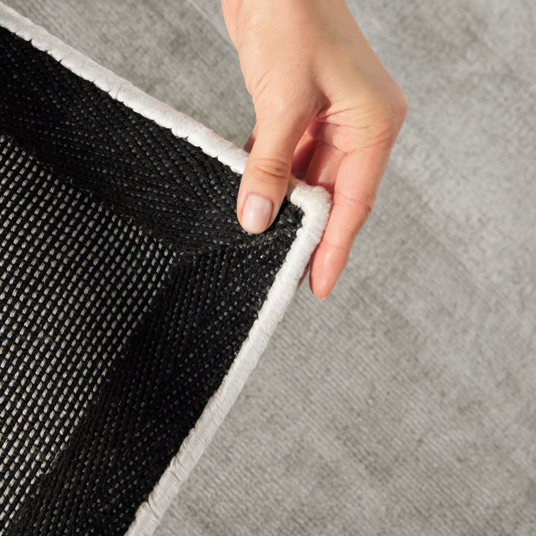 Person peeling back a gray rug to reveal black underlay