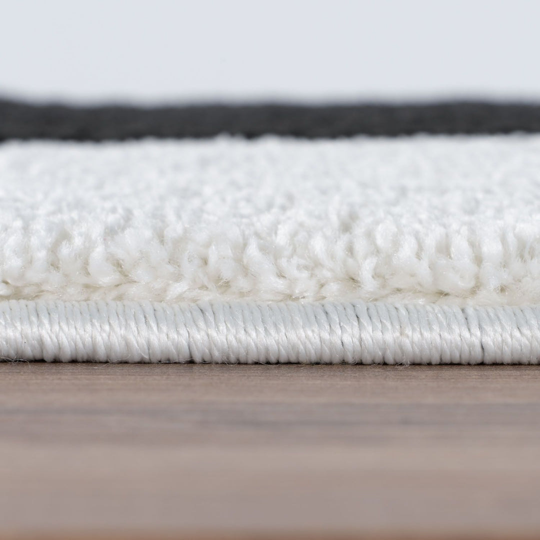 Close-up of a textured white rug on a wooden floor with a light gray background