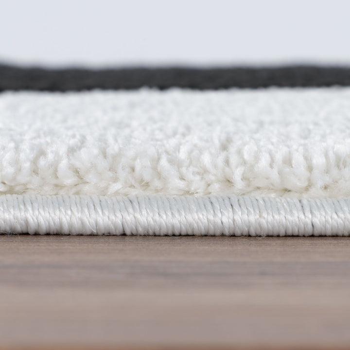 Close-up of a textured white rug on a wooden floor with a light gray background