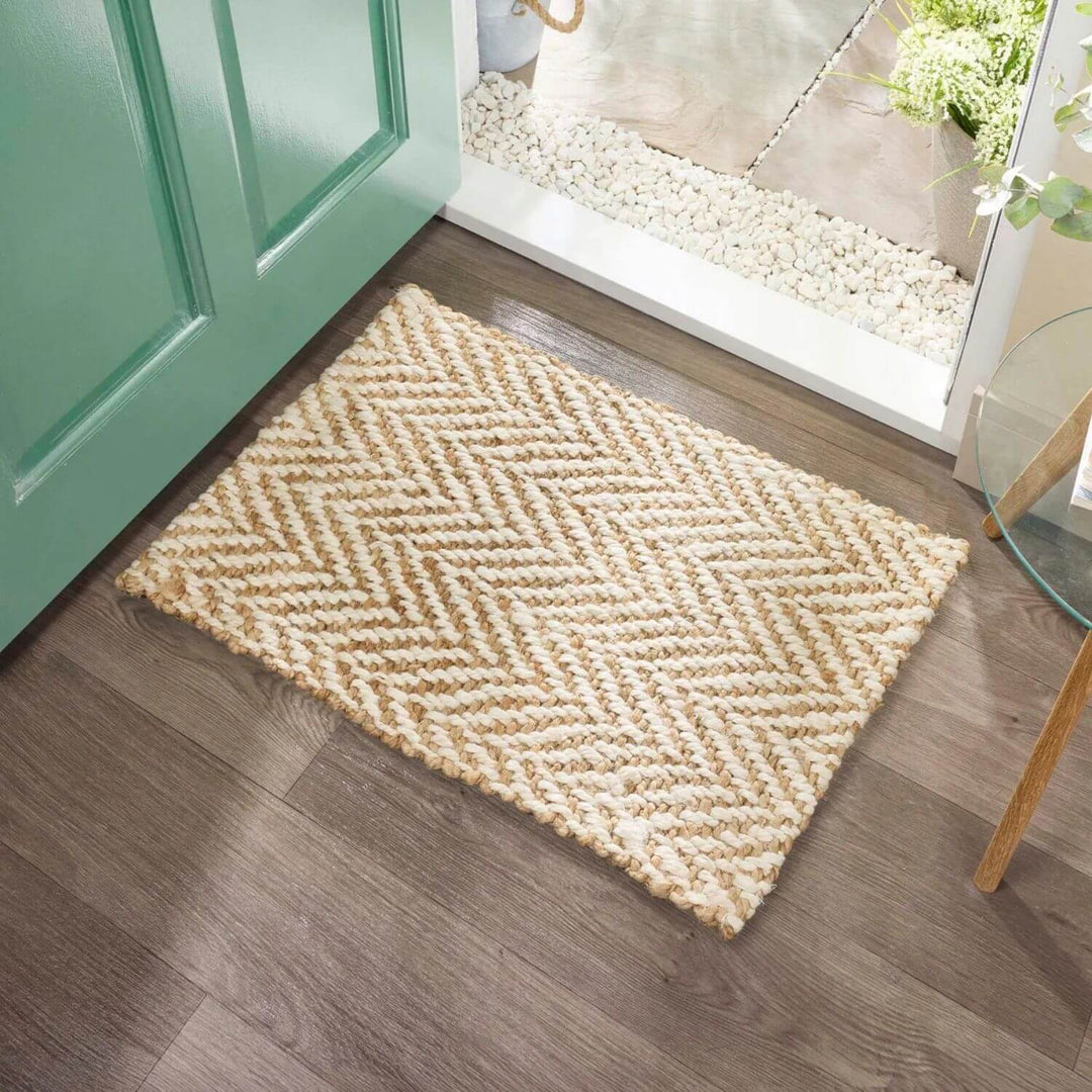 Beige doormat with a zigzag pattern on a wooden floor in front of a green door.