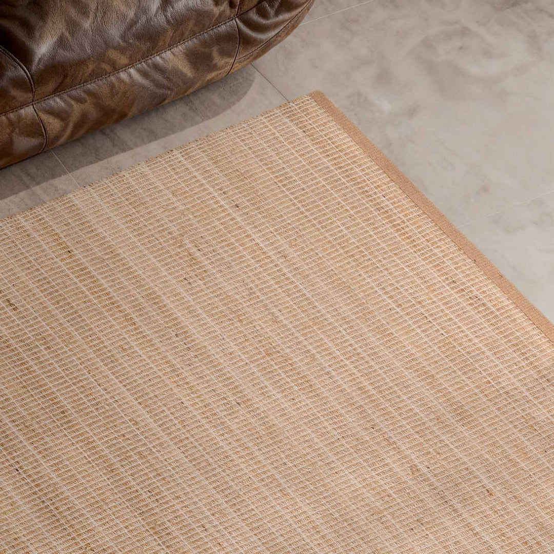 Beige woven mat on a concrete floor with a brown leather chair corner.