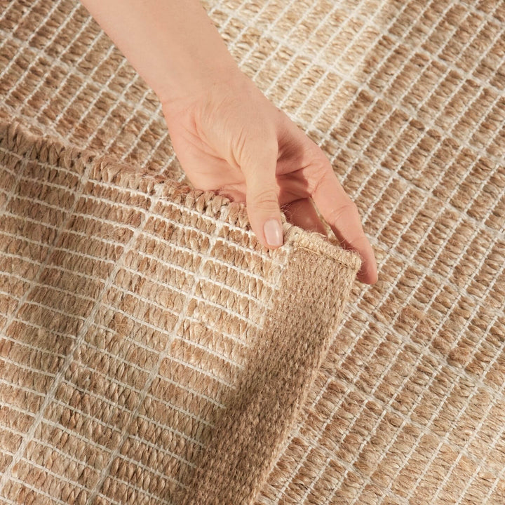 Hand holding a corner of a textured beige rug