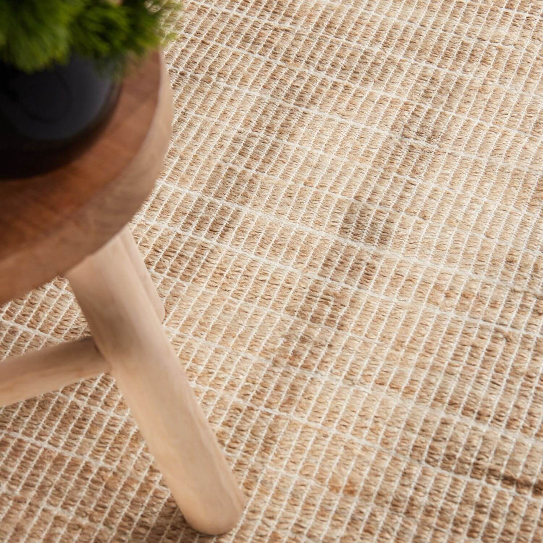 Close-up of a textured beige rug with a wooden stool and plant in the corner.