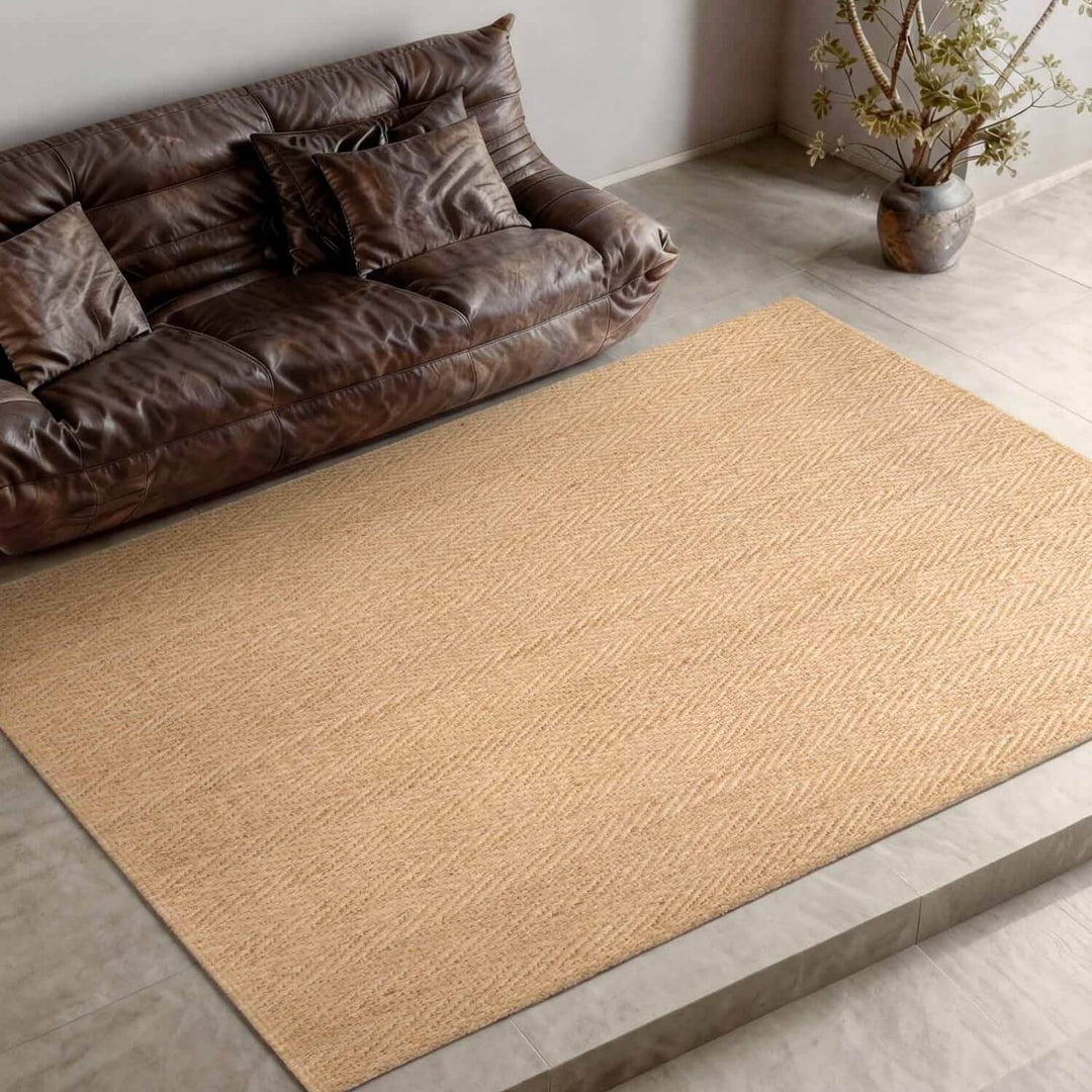 Brown woven rug on a wooden floor with a brown sofa and plant in the background.