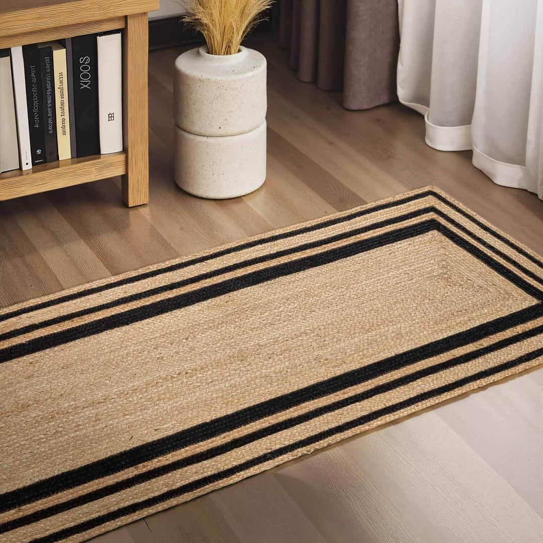 Beige rug with black stripes on a wooden floor, next to a bookshelf and plant.