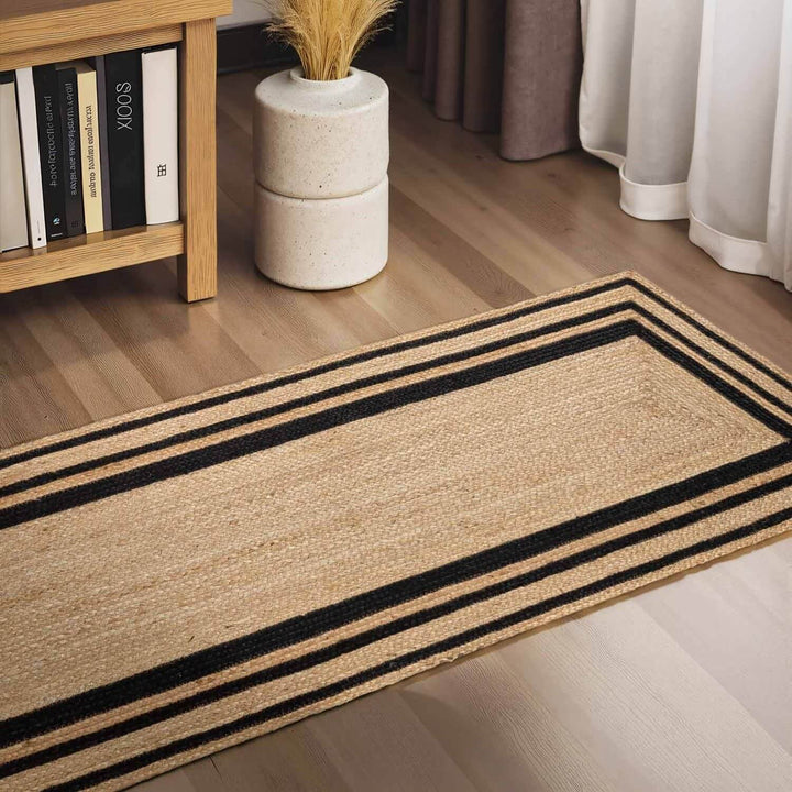 Beige rug with black stripes on a wooden floor, next to a bookshelf and plant.