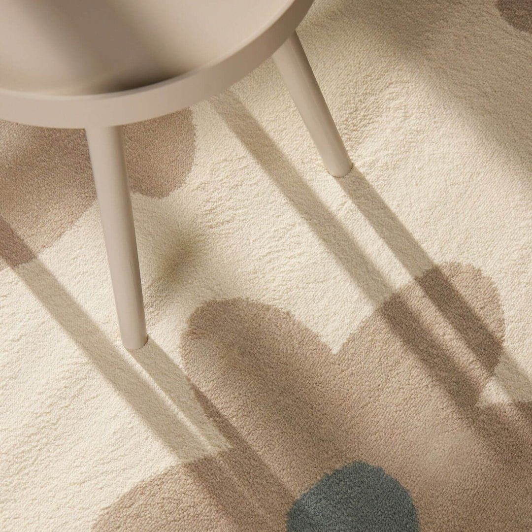 Beige carpet with abstract patterns and a white chair leg casting a shadow.