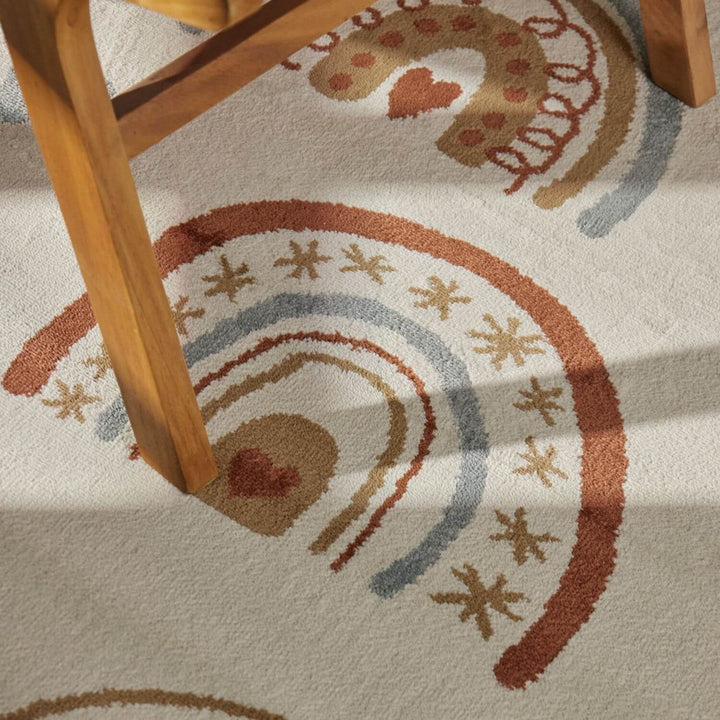 Close-up of a patterned rug with rainbow and heart design, partially covered by a wooden chair.