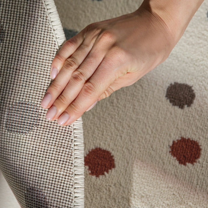 Hand touching a textured fabric surface with a pattern of brown dots.