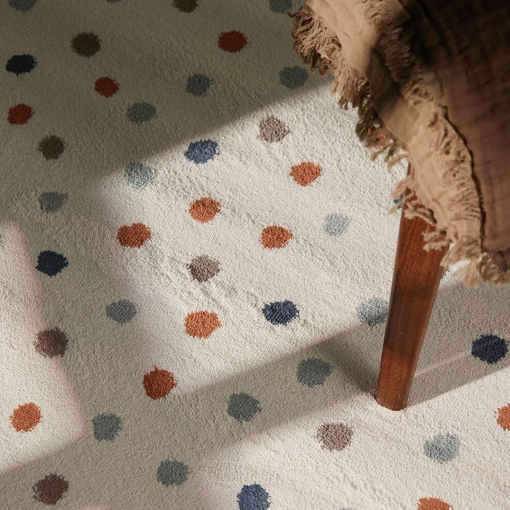 Close-up of a polka dot rug with a wooden chair leg and textured fabric corner.