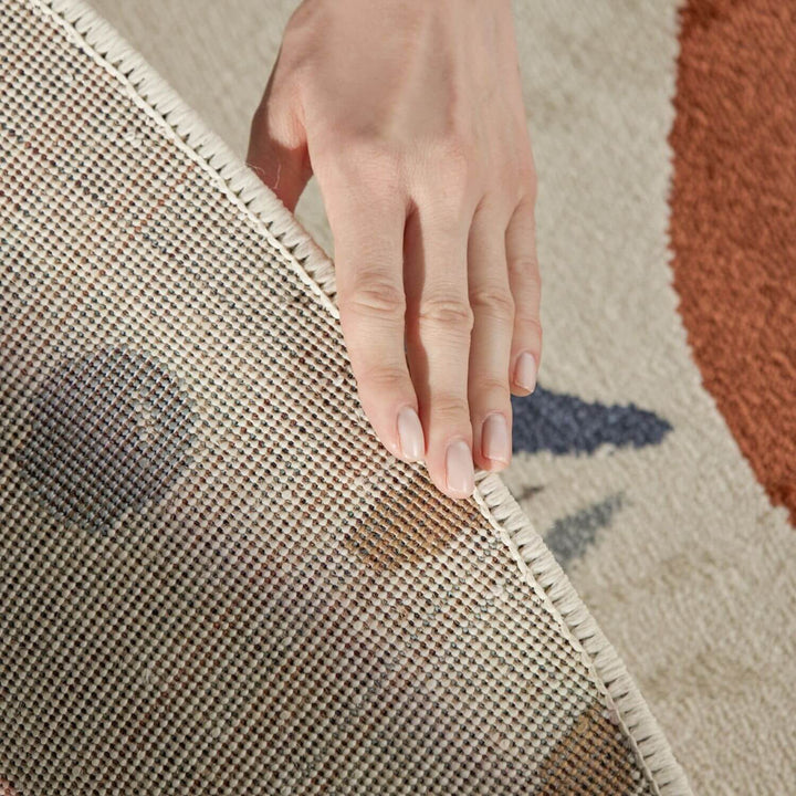 Hand touching the edge of a textured rug with a geometric pattern