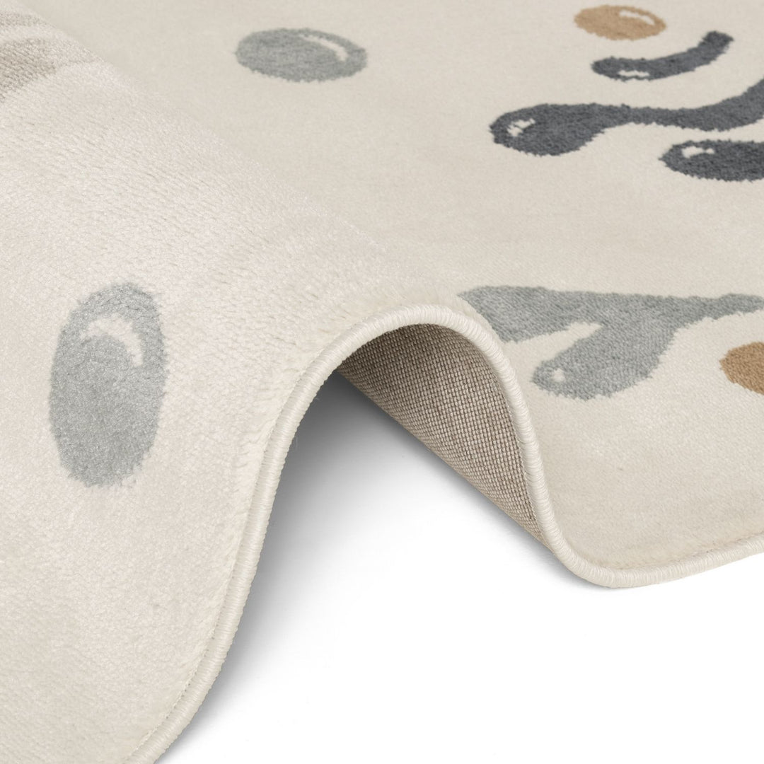 Close-up of a beige rug with abstract black, gray, and brown shapes on a white background