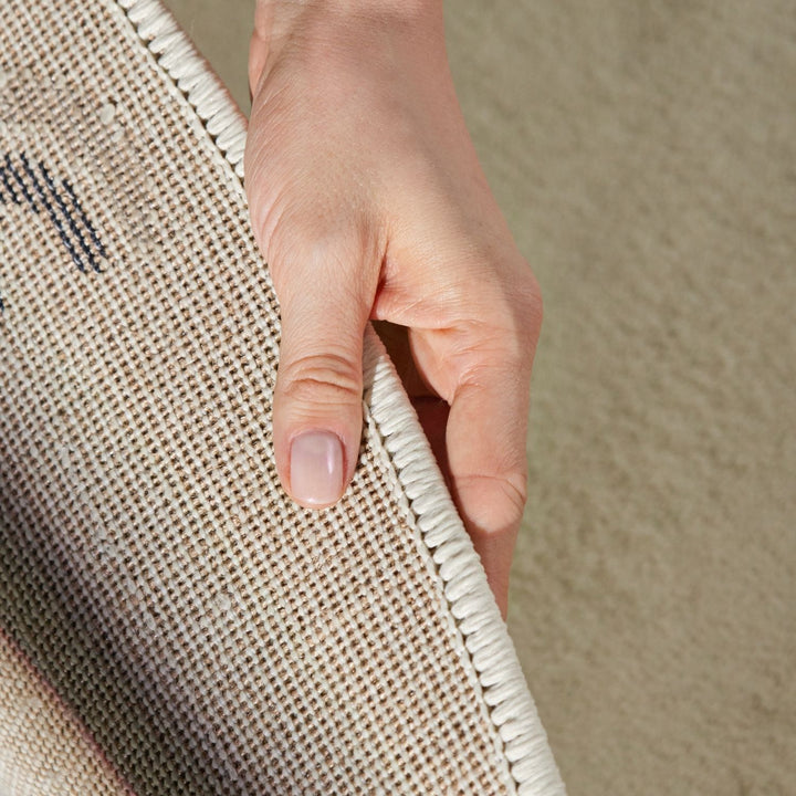 Hand holding a textured beige rug corner on a matching beige background