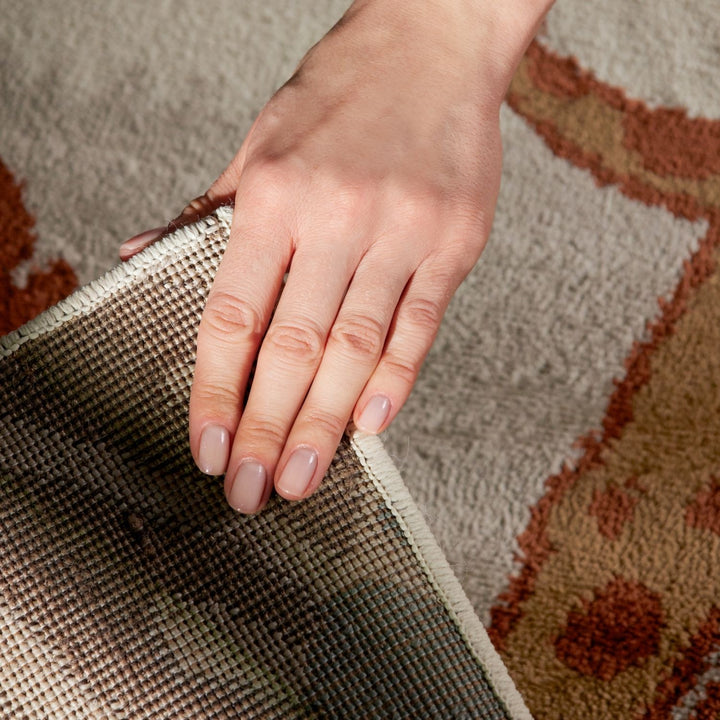 Hand pulling a rug off the floor with a patterned rug underneath