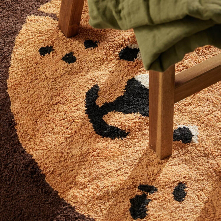 Round brown rug with black paw prints on a brown floor.