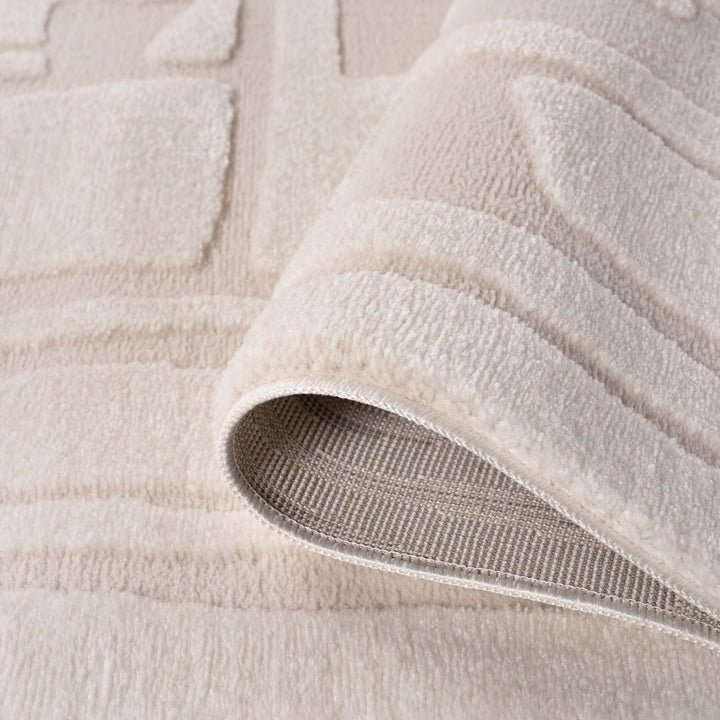 Close-up of a beige textured rug with a slight roll-up showing the underlayer.