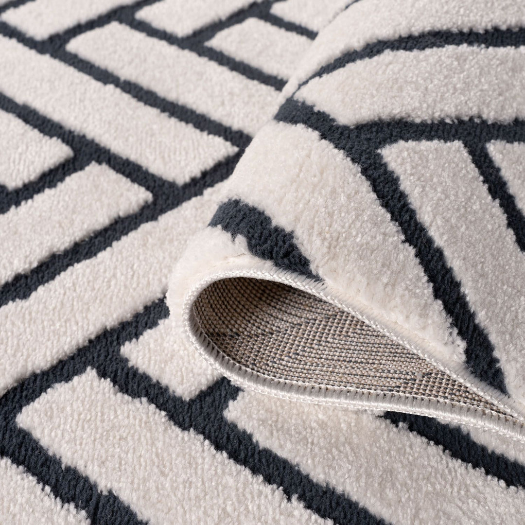 Close-up of a textured rug with geometric pattern and a part of a shoe visible.