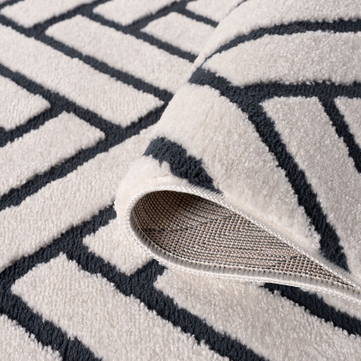 Close-up of a textured rug with geometric pattern and a part of a shoe visible.