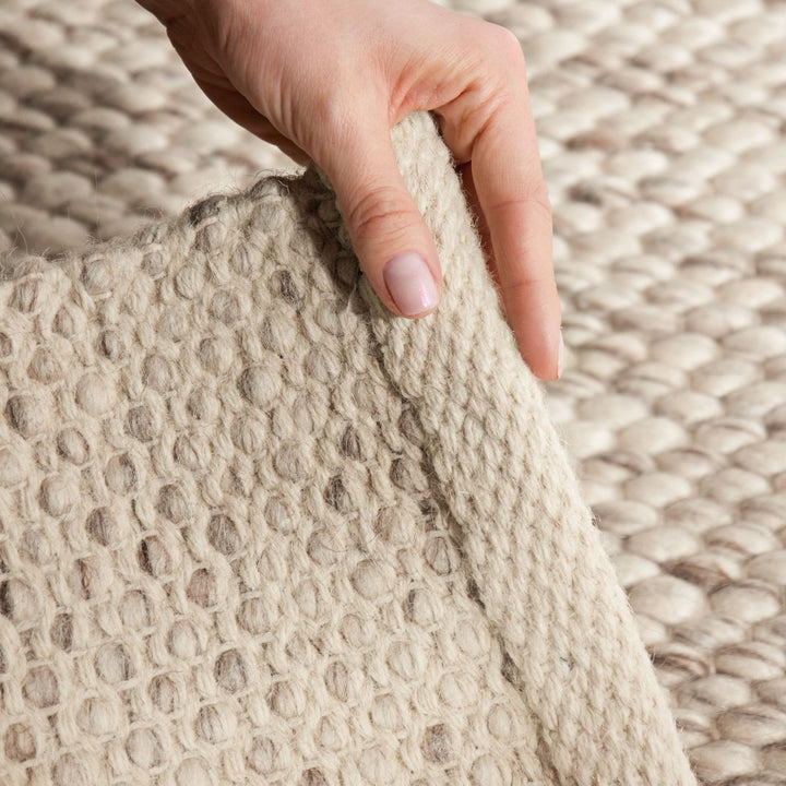 Close-up of a hand touching a textured beige fabric against a matching fabric background