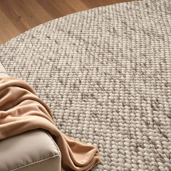 Beige rug on a wooden floor with a beige couch corner.