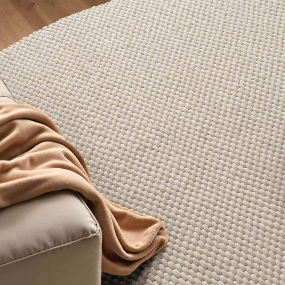 Beige textured rug with a corner of a beige sofa and a beige blanket.