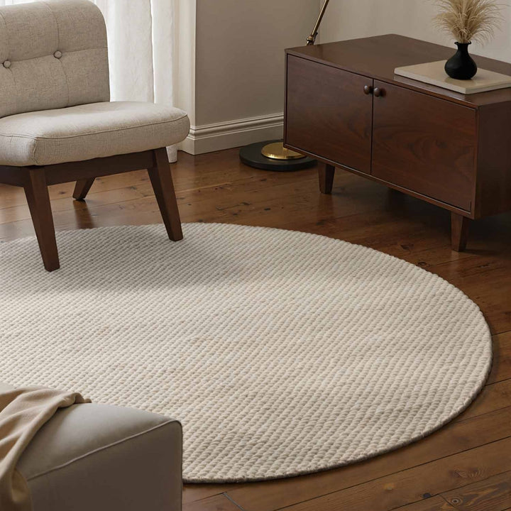 Round beige rug in a living room with wooden furniture and a beige armchair.