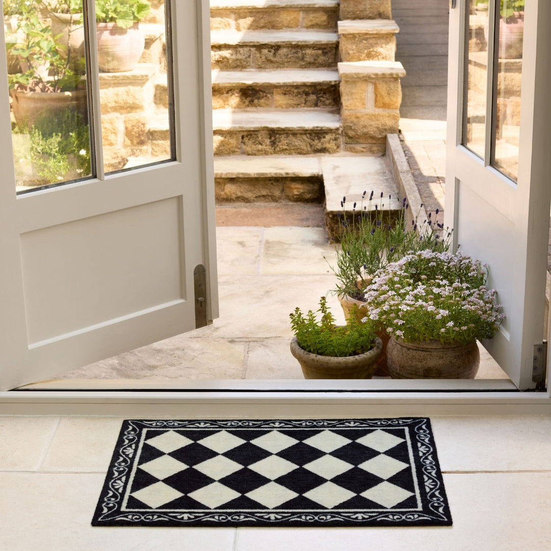 Decorative checkered mat in front of a glass door with plants and steps outside.