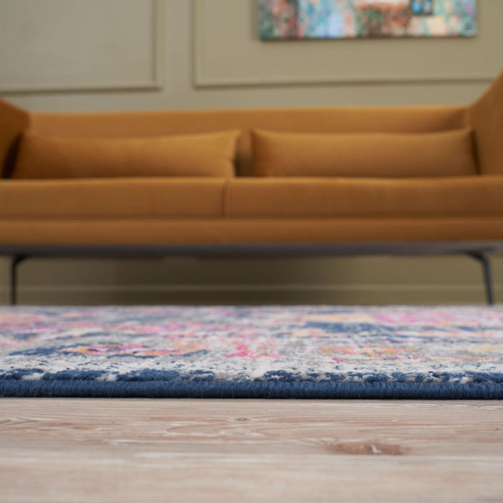 Multicolored patterned rug on a wooden floor with a blurred brown sofa in the background.