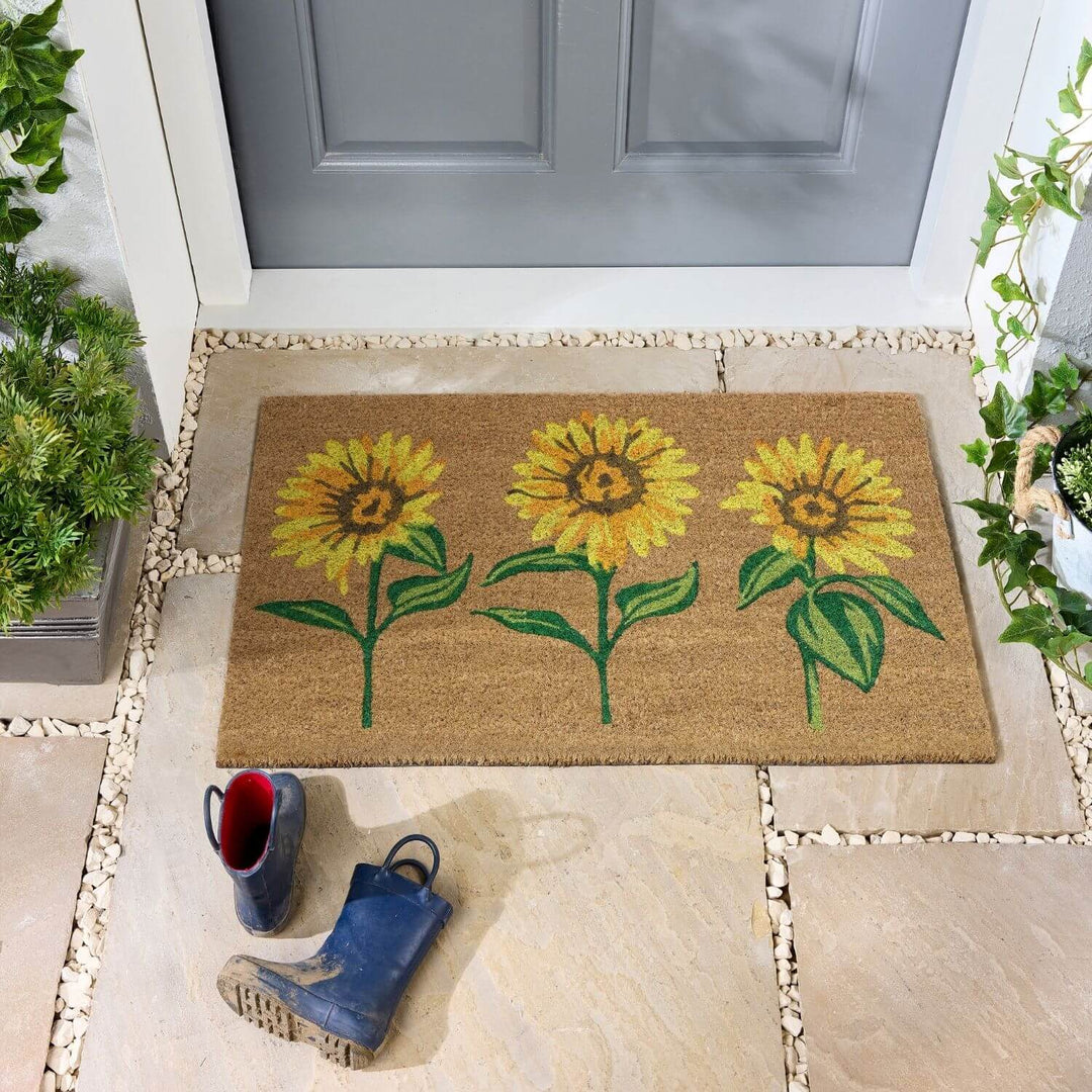 Doormat with sunflower design on a stone pathway leading to a door.