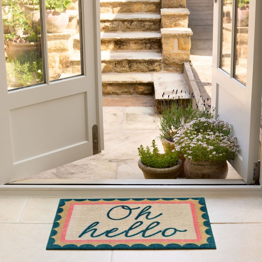 Doormat with 'Oh hello' text in front of a house entrance with plants and steps.
