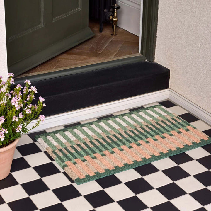 Doormat with geometric pattern on a checkered floor in front of a door.