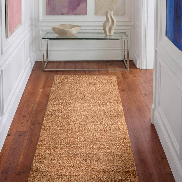 Long beige rug on a wooden floor with a glass table and decorative items in the background.