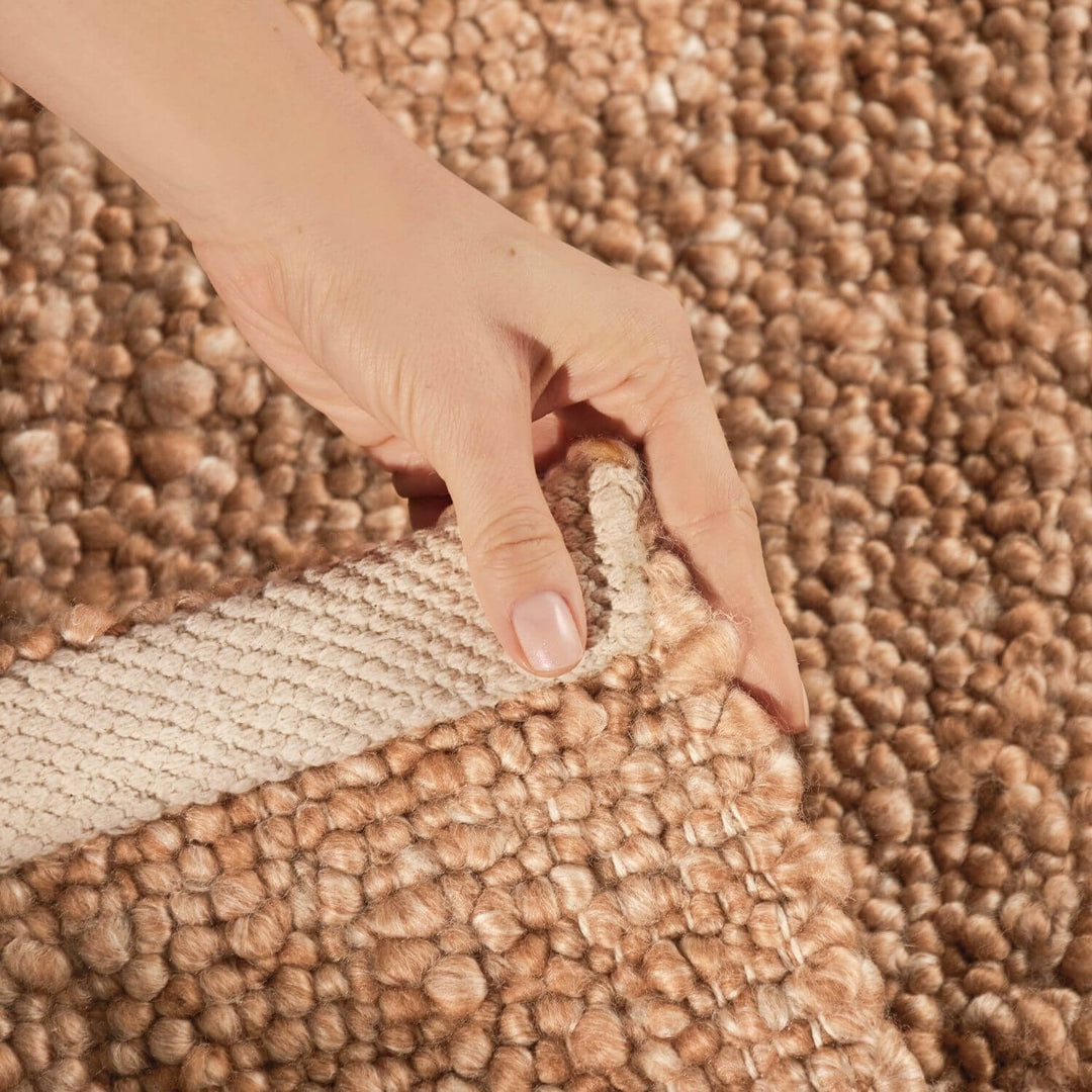 Hand pulling a strip of brown carpet to reveal a lighter color underneath