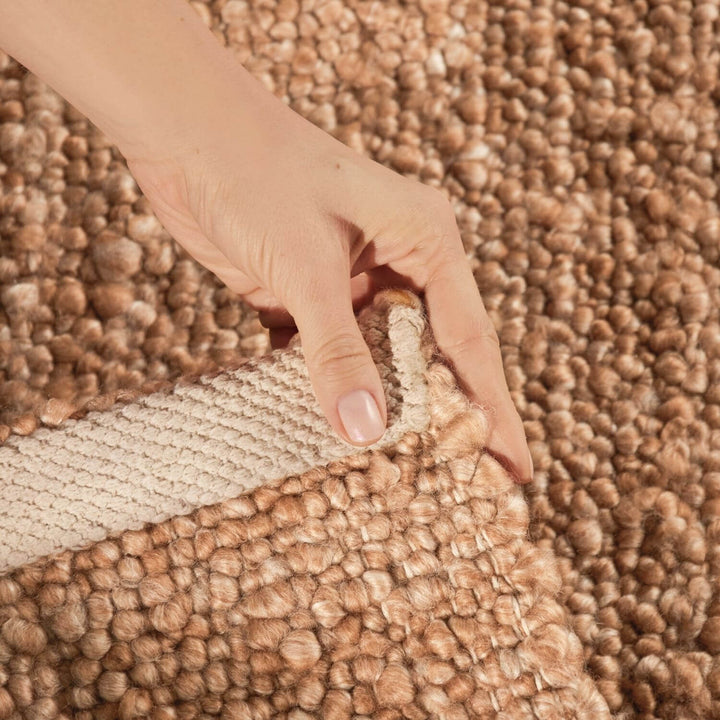 Hand pulling a strip of brown carpet to reveal a lighter color underneath