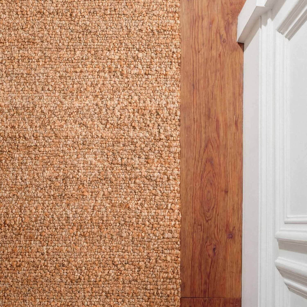 Close-up of a carpeted floor transitioning to a wooden floor with a white baseboard.