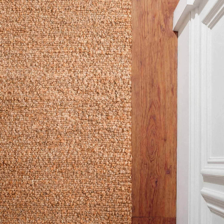 Close-up of a carpeted floor transitioning to a wooden floor with a white baseboard.