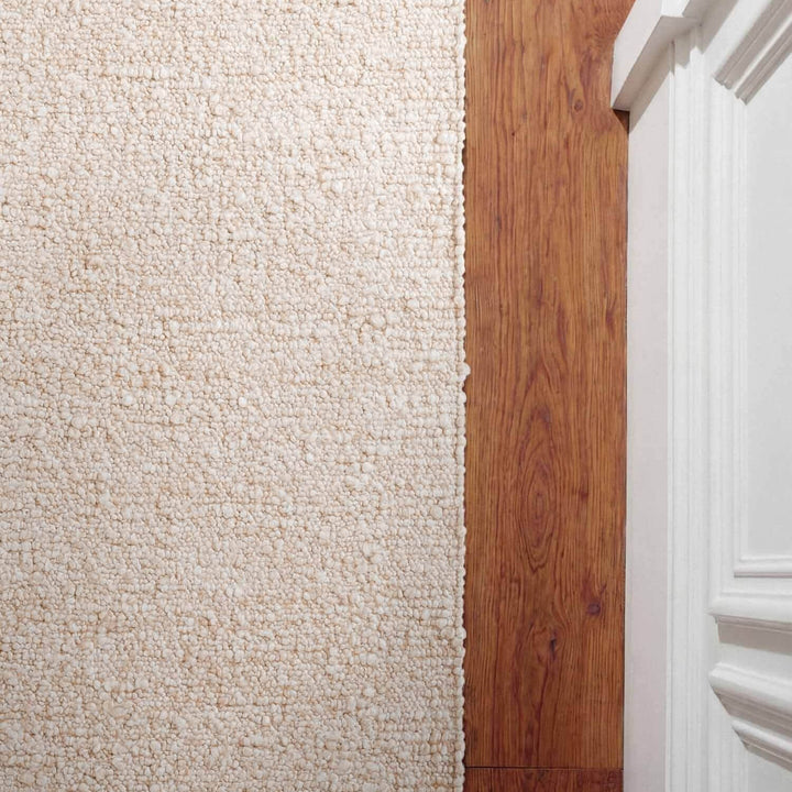 Close-up of a carpeted floor transitioning to a wooden floor with a white baseboard.