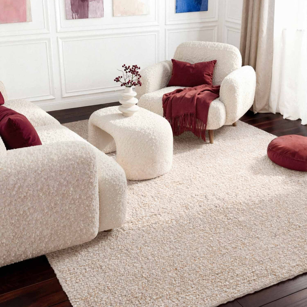 Living room with white armchairs, a round ottoman, and red cushions.