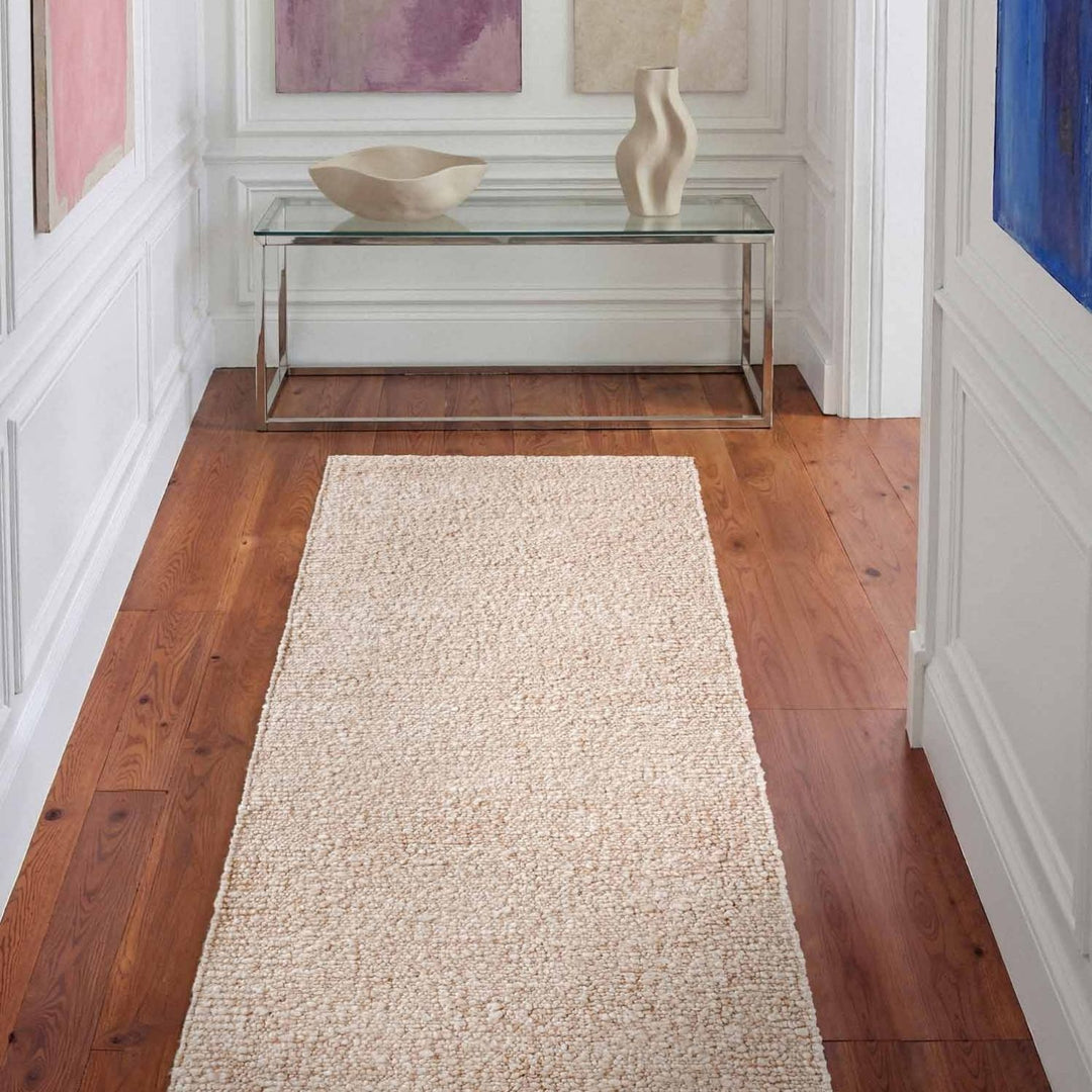 Beige runner rug on a wooden floor with a glass table and decorative items in the background.