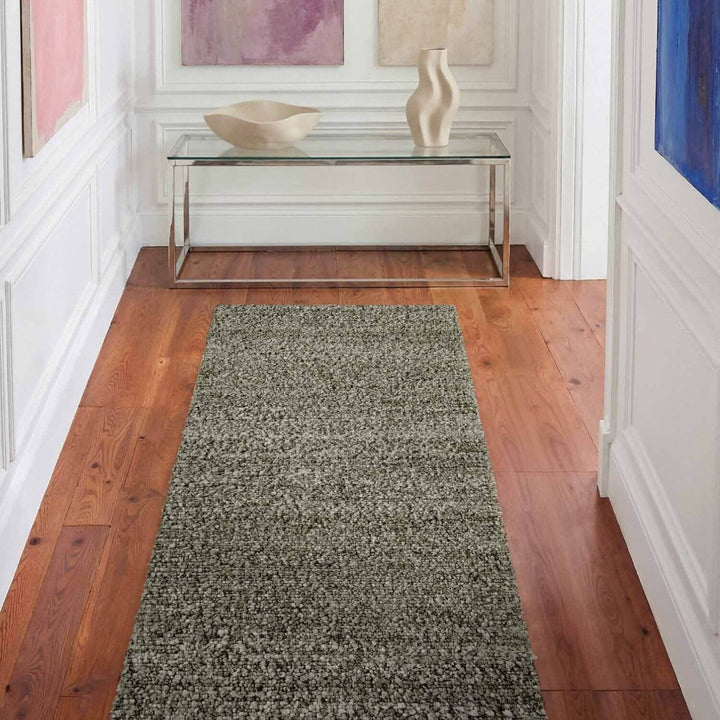 Gray runner rug on a wooden floor with a glass table and decorative items in the background.
