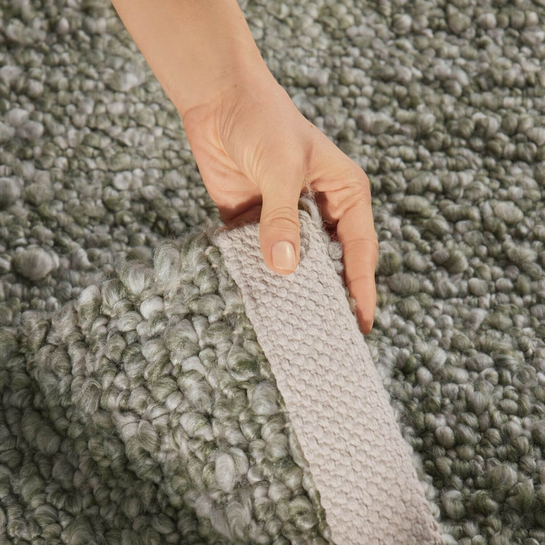 Person holding a textured gray carpet sample against a matching green carpet background