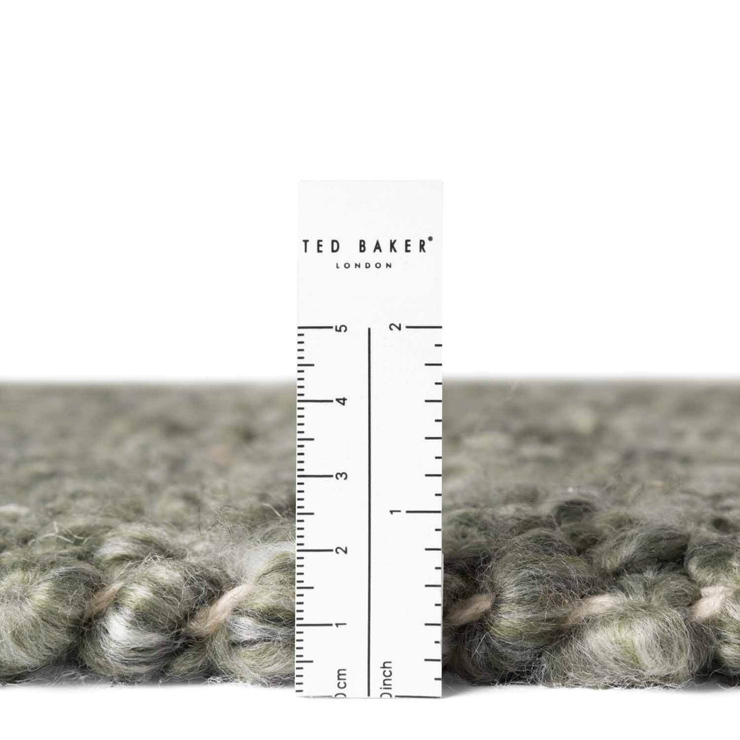 Close-up of gray yarn with a ruler and 'Ted Baker London' label on a white background