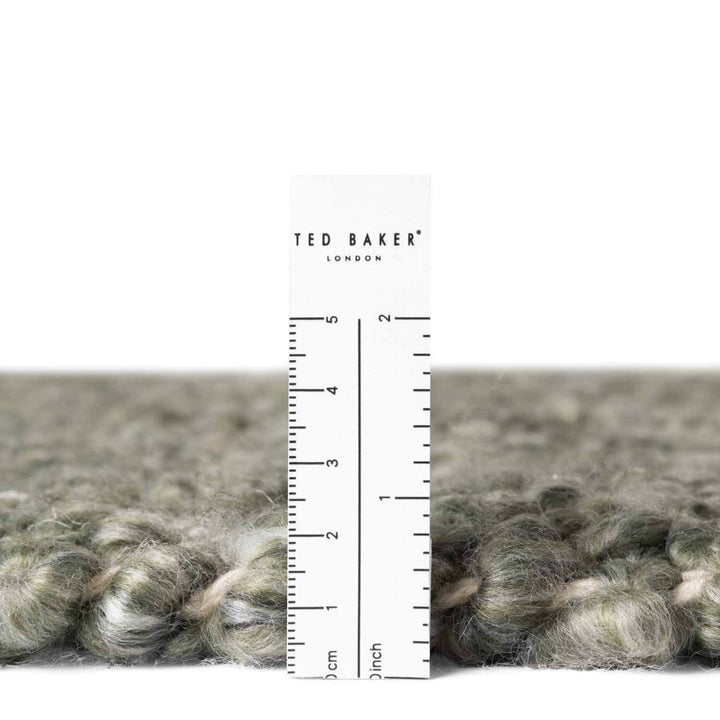 Close-up of gray yarn with a ruler and 'Ted Baker London' label on a white background