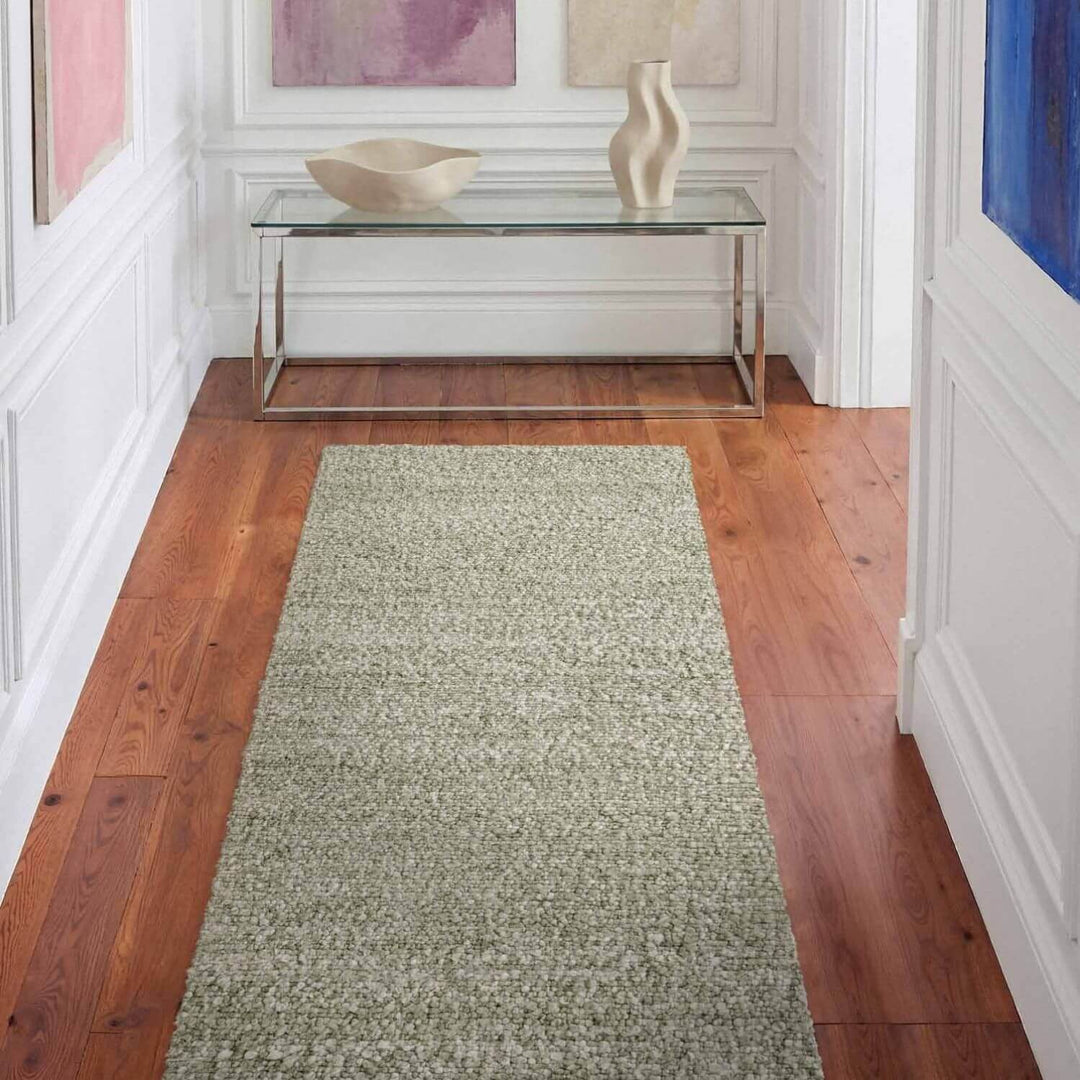 Green runner rug on a wooden floor with a glass console table and decorative items.