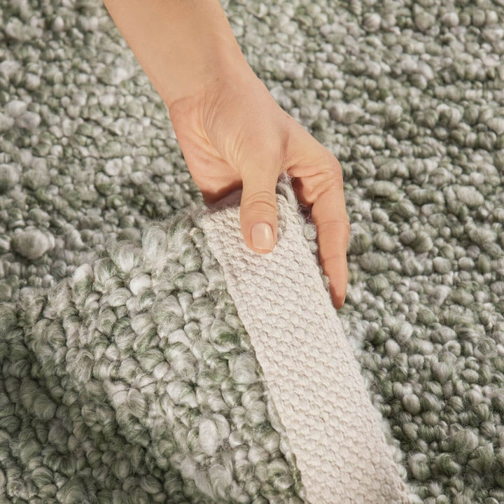 Hand holding a textured gray carpet sample against a matching carpet background
