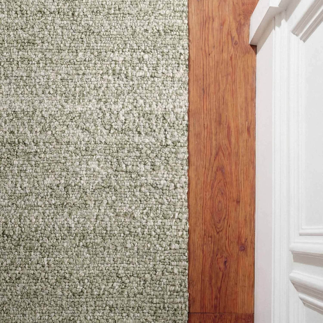 Close-up of carpeted floor transitioning to wooden flooring with a white baseboard.