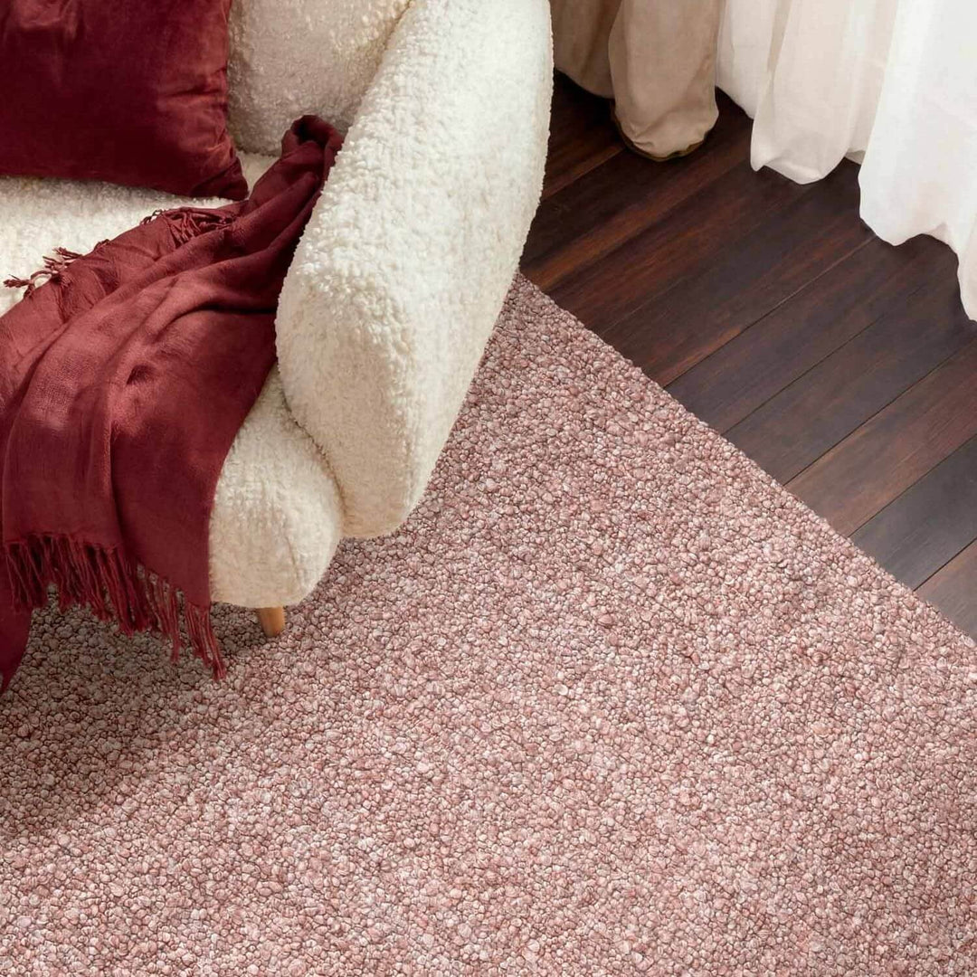 Close-up of a textured pink carpet with a white sofa and red blanket in the background.